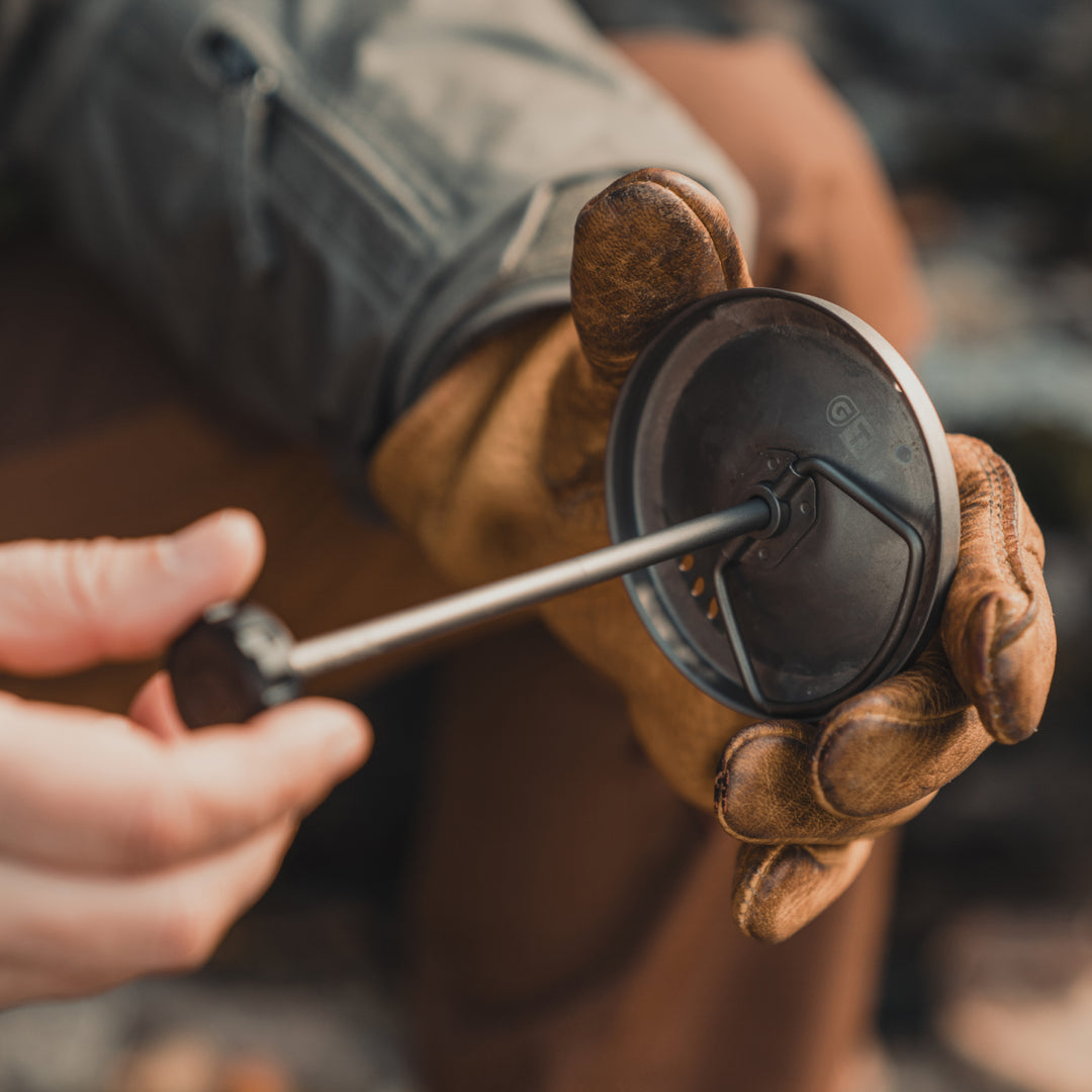 Person wearing a leather glove handling a Grayl Titanium Coffee Press (aka French Press) for their GeoPress Ti